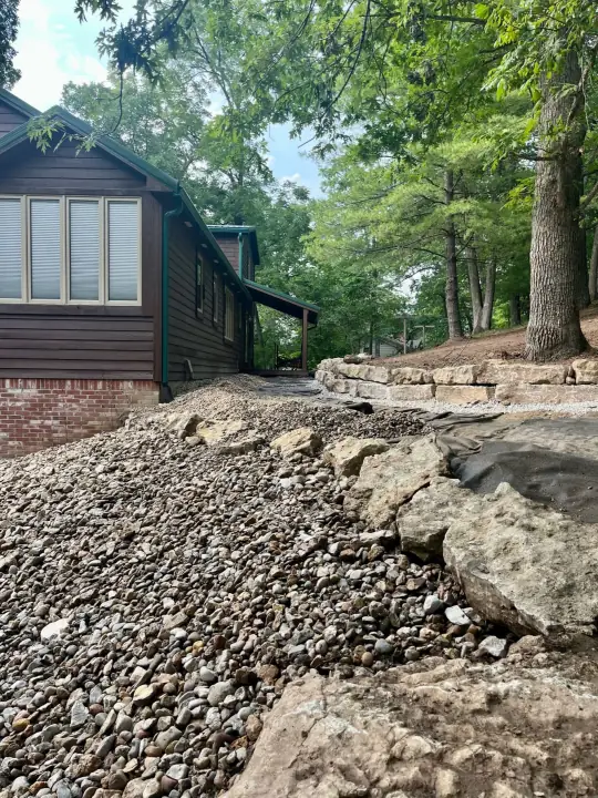 A natural stone wall and gravel border beside a dark wooden cabin in the woods