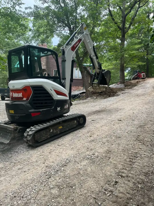 A compact excavator on a gravel drive beside a house