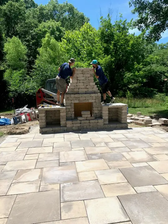 Two workers building a stacked block outdoor fireplace on a new paver patio