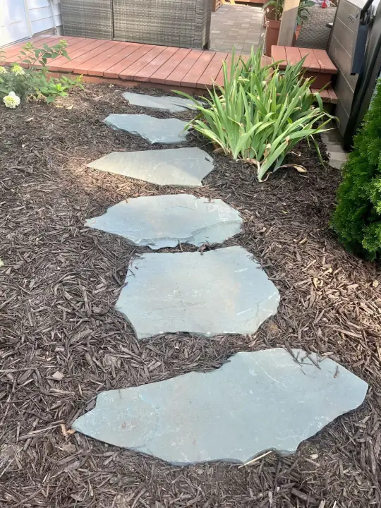 Irregular flagstone stepping stones set in mulch leading to a deck, with lilies beside them