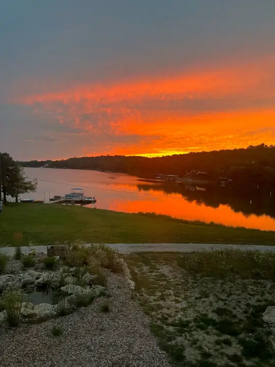 A vivid orange sunset reflected in a lake above a planted slope