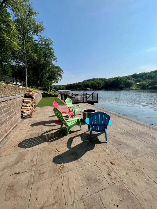 Colorful Adirondack chairs and a fire bowl on a lakeside patio beside a block retaining wall