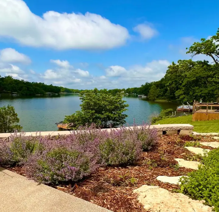 Purple lavender and flagstone beside a lawn sloping down to a lake
