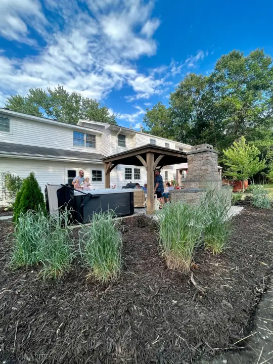 Ornamental grasses and new planting in front of a pavilion and a white house under a blue sky