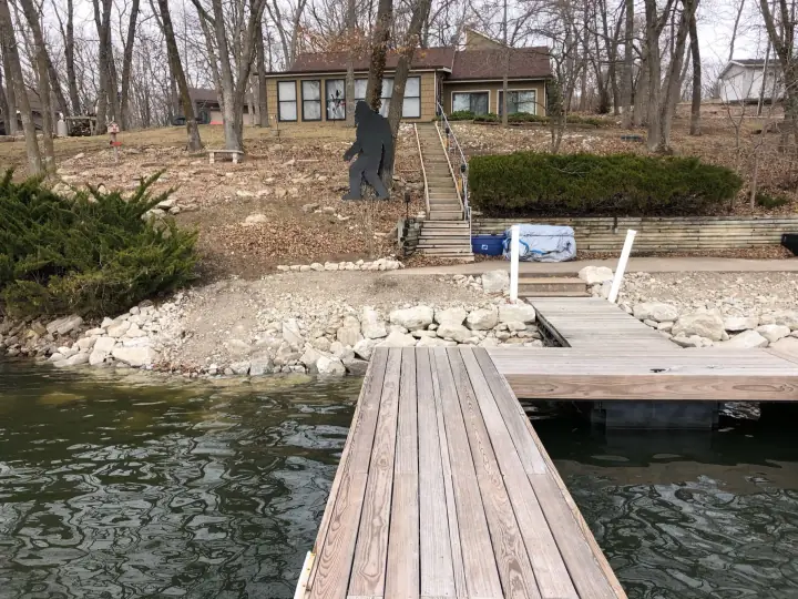 A dock on a lake, a stone-armored shoreline and steps up to a house among bare trees
