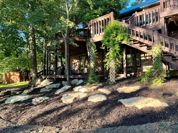 Flat stone stepping pads in dark mulch beneath a tall wooden deck and stairs