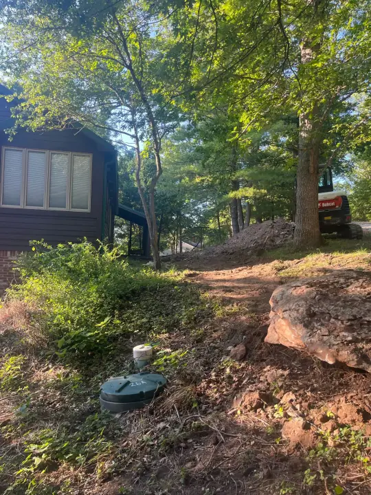 A stacked stone wall and new shrubs along the side of a cabin among trees