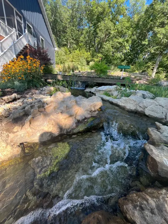 Water tumbling over natural stone ledges in a stream edged with boulders and orange flowers